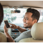 Contabilidade TVDE: Como Funciona o Regime IVA para Motoristas? Contabilidade TVDE: Motorista mulher usando aplicação enquanto passageira entra no carro, representando serviços de contabilidade especializados para motoristas TVDE.